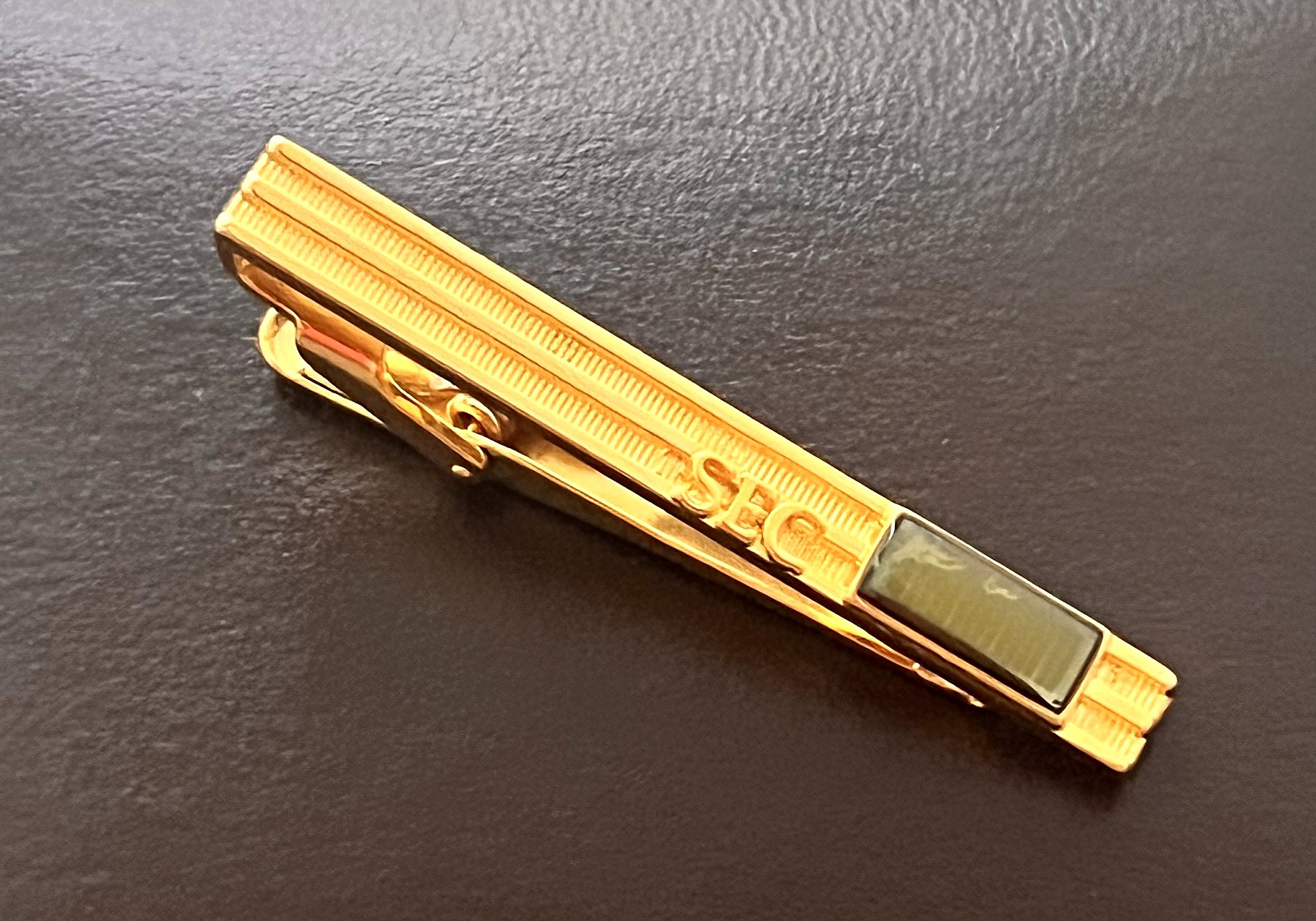 A gold plated tie clip marked SEC, with a small silicon chip set under a clear window at one end